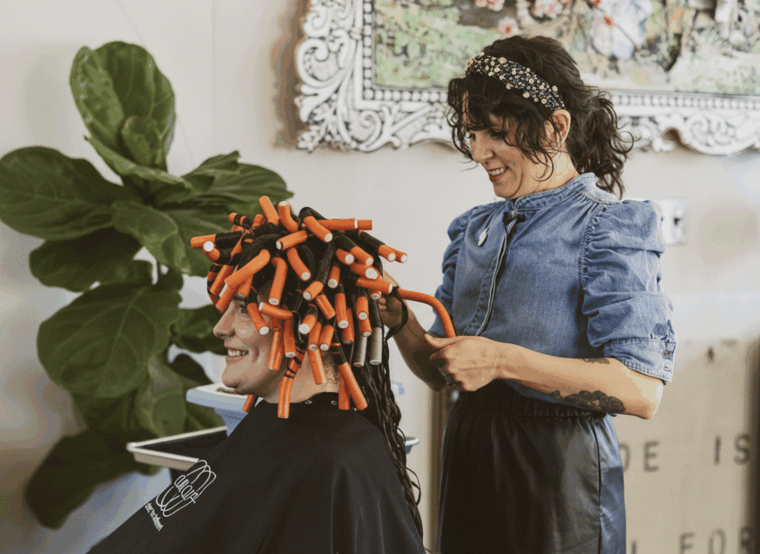 Hair stylist applying foam rollers to curly hair for volume.